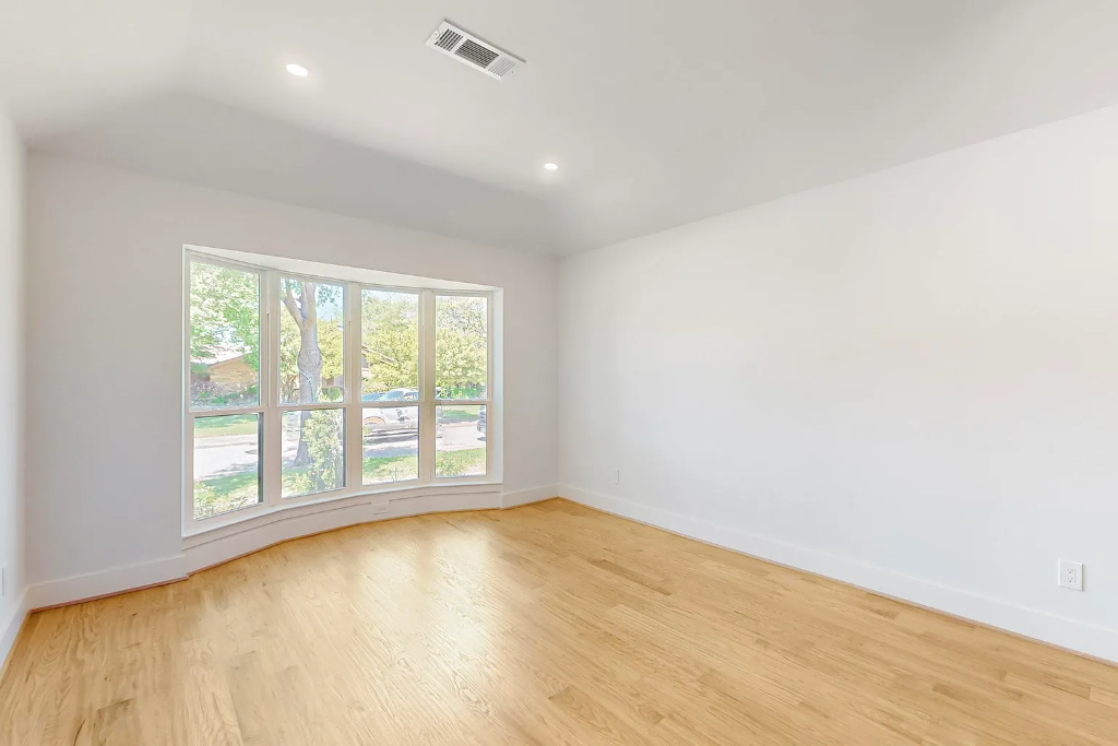 Sunlit room with a curved bay window and pristine newly installed light oak hardwood flooring reflecting natural light in a DFW home remodel by 448 Developments