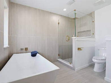 Bathroom remodel with standalone soaking tub, glass enclosed walk-in shower, large format neutral tile and gold fixtures in DFW area