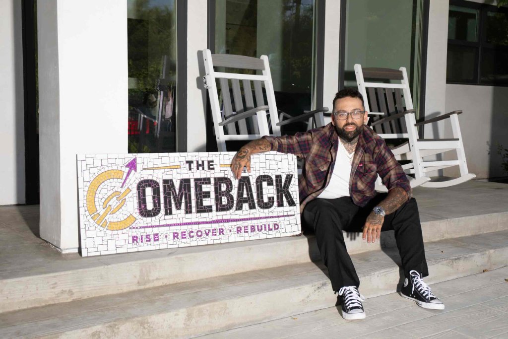 Vinny, founder of The Comeback Sober Living, seated with The Comeback mosaic sign on the steps of the men's sober living home in Van Nuys CA — Rise Recover Rebuild