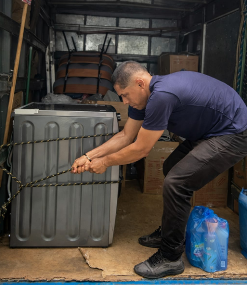 Equipe própria fixando eletrodoméstico com cinta no caminhão baú durante mudança residencial