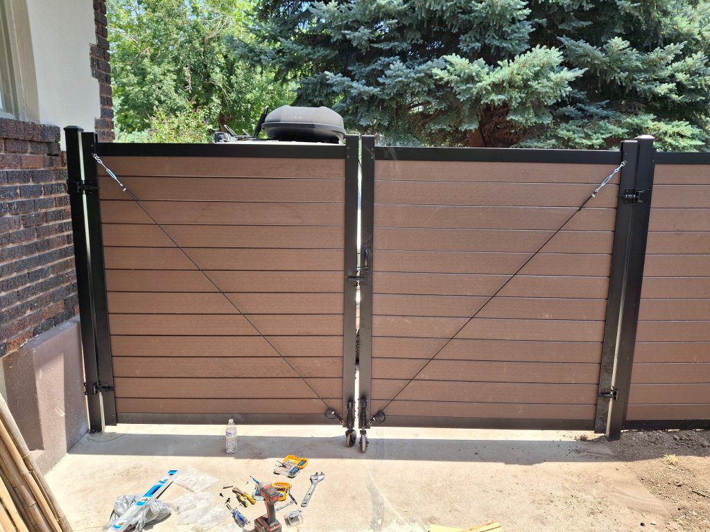 Composite wood-look double gate with black metal frame, diagonal cable tensioners and caster wheels