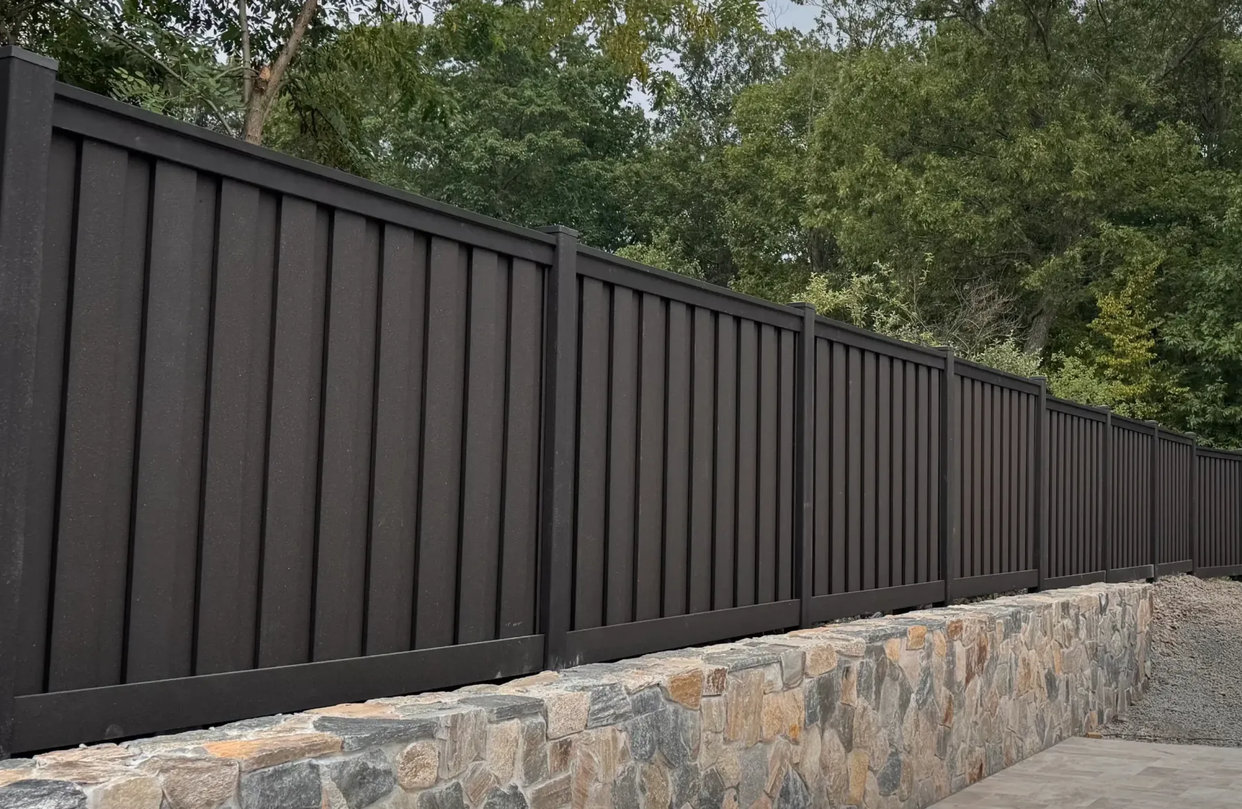 Dark charcoal Trex composite privacy fence installed on stone retaining wall