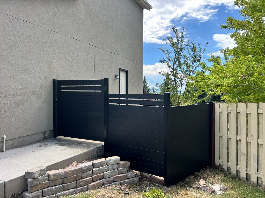 Black horizontal-slat privacy screen installed beside a beige stucco home