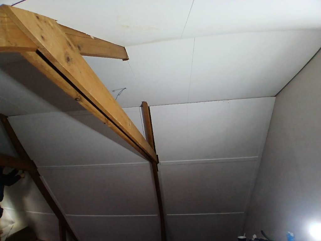 Afgewerkt plafond met witte panelen tussen de spanten