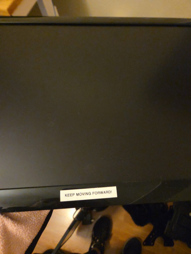 A label taped to Ian's monitor reading KEEP MOVING FORWARD!