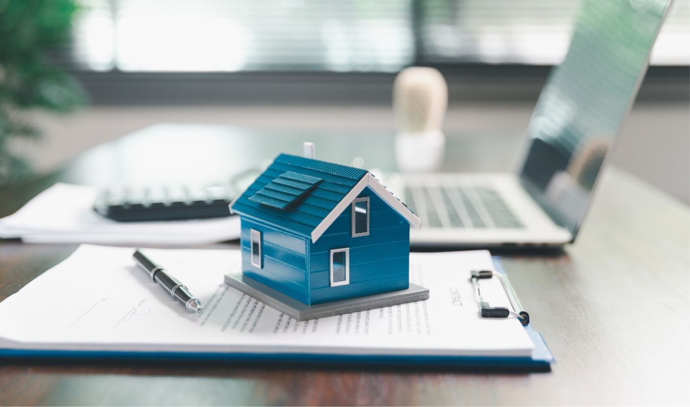 A model house on mortgage paperwork beside a laptop
