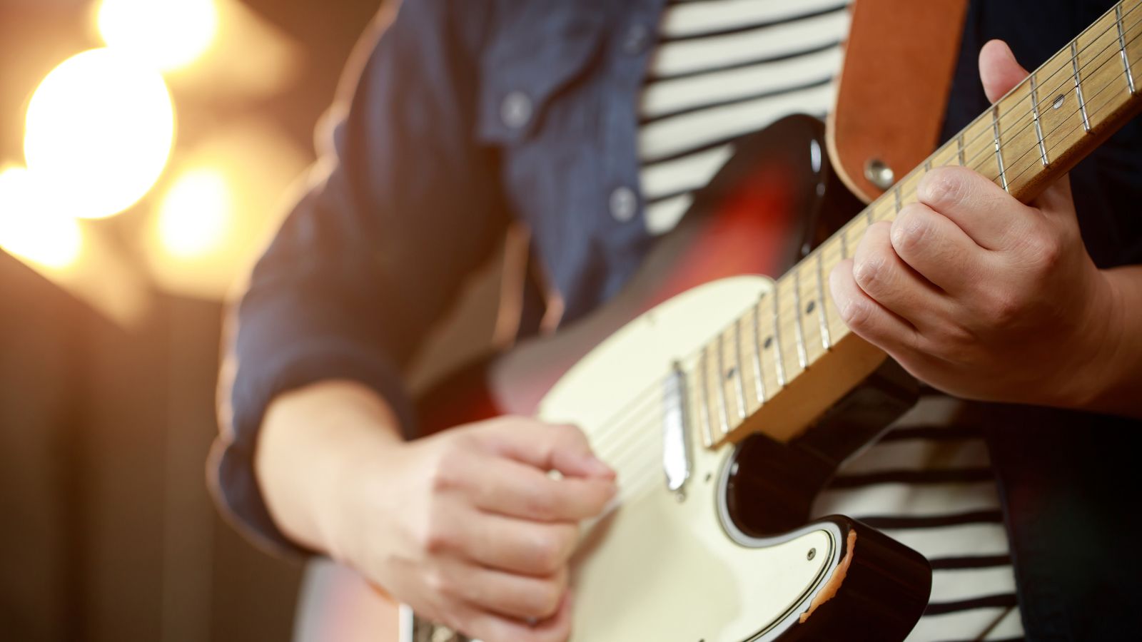 Close-up of a musician playing an electric guitar under warm stage lighting. Real photograph from Canva by rattanakun.