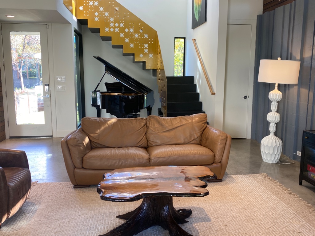 Grand living room with leather sofa, gold staircase, and grand piano