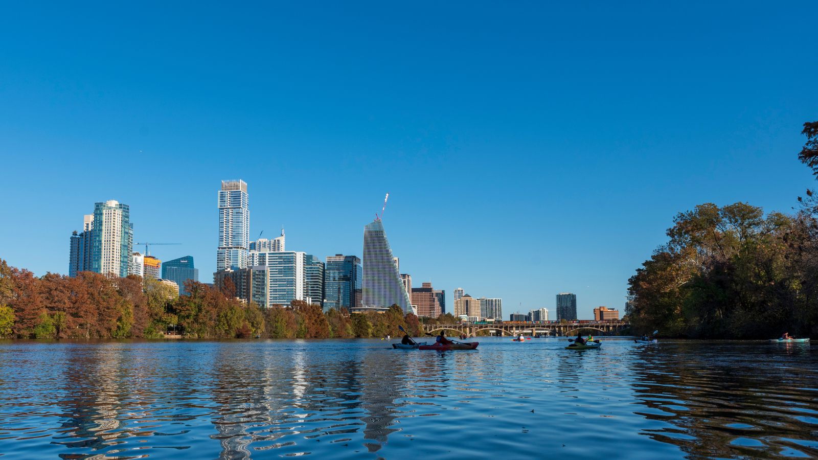Kayakers on Lady Bird Lake with the Austin skyline. Real photograph by Trac Vu / Pexels, sourced through Canva.