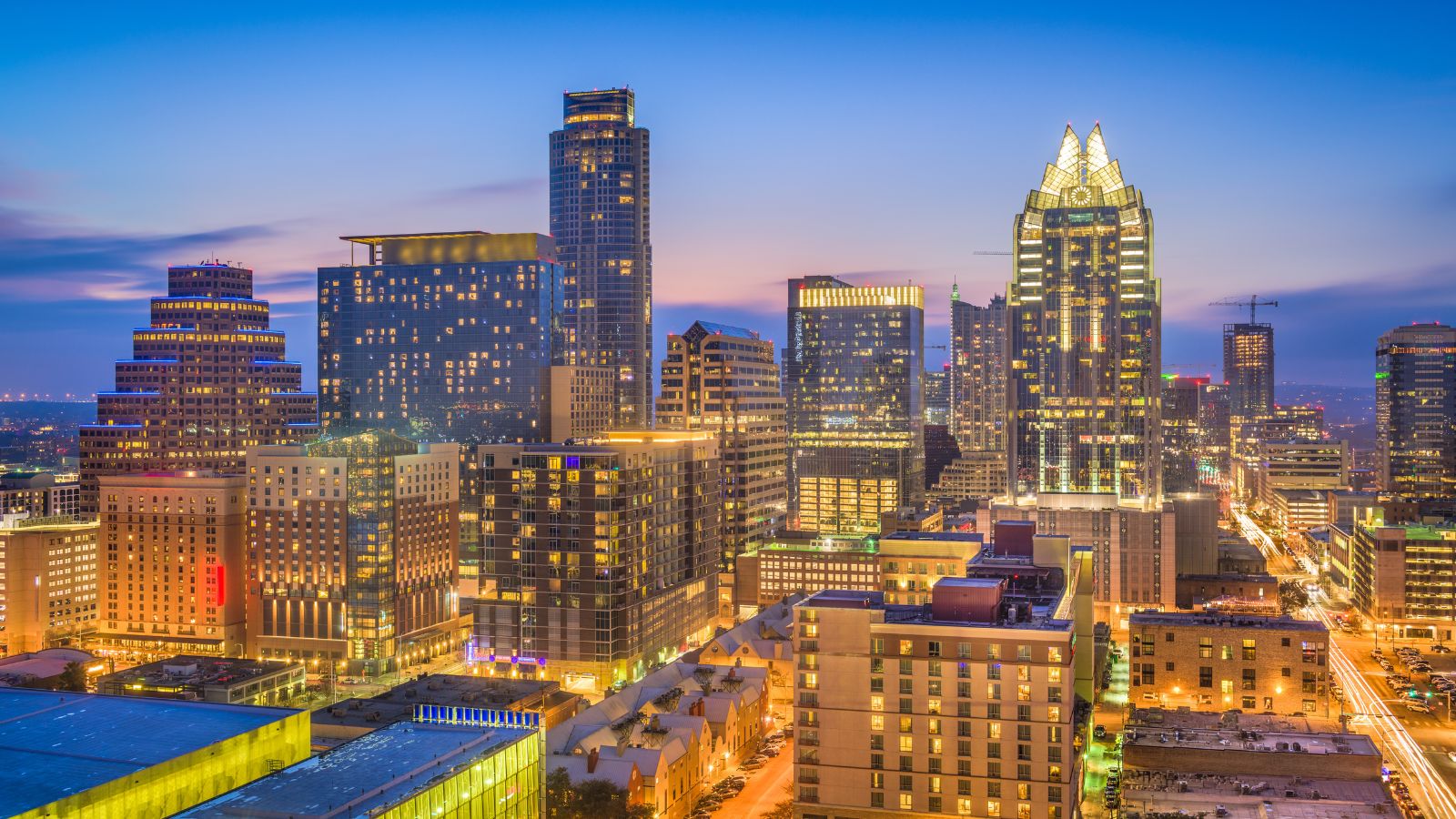 Downtown Austin at dusk with the illuminated Frost Bank Tower and Congress Avenue. Real photograph by Sean Pavone / Getty Images, licensed through Canva.
