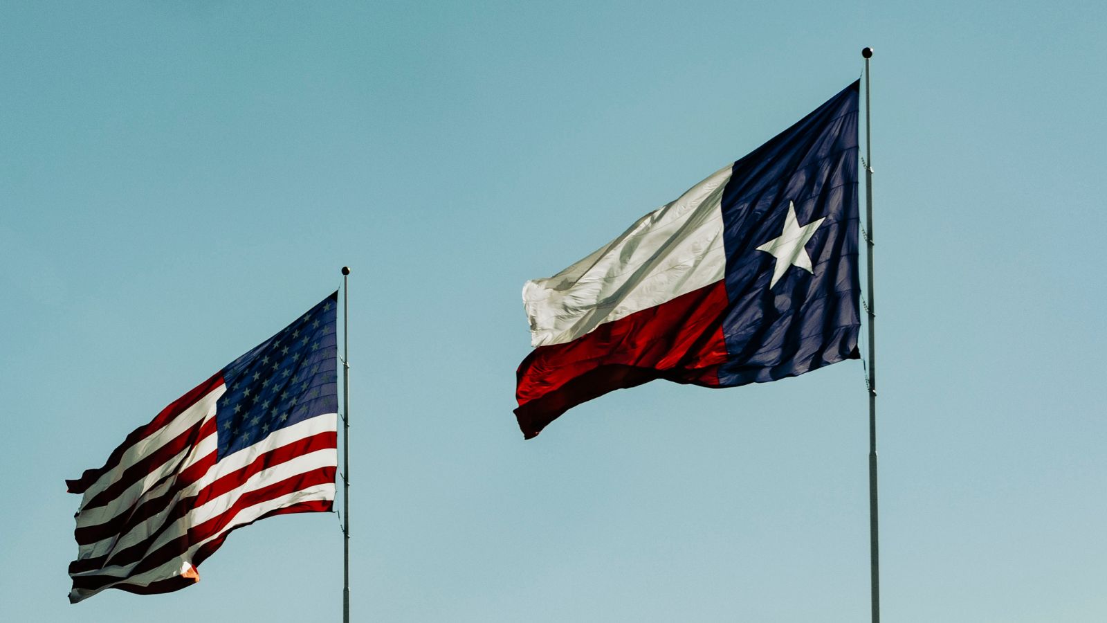 Texas and United States flags against a blue sky. Real photograph by Talena Reese.