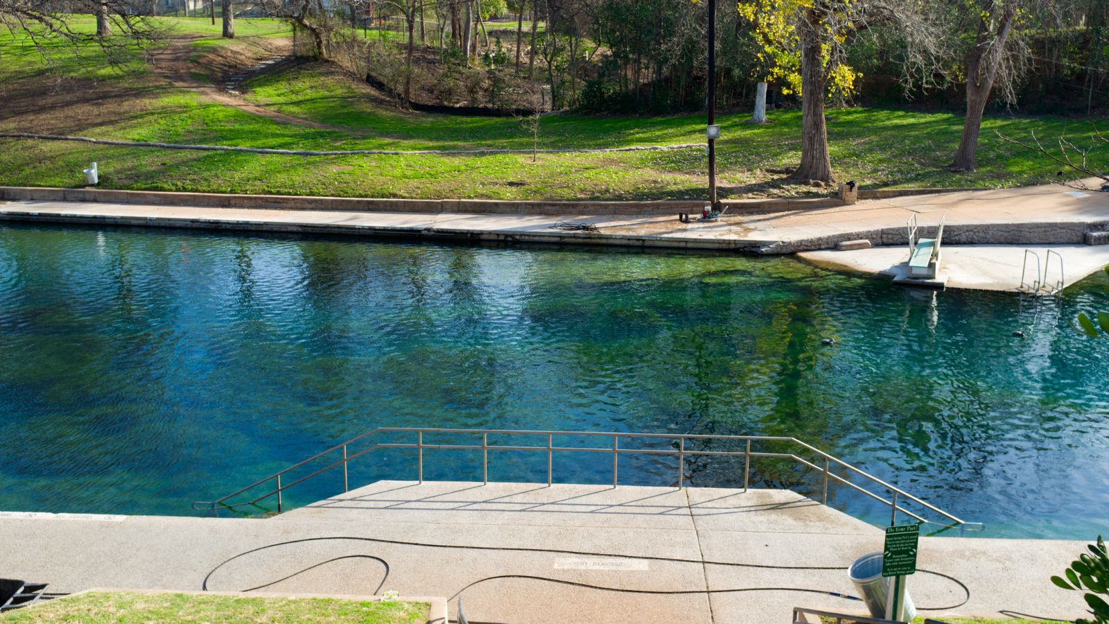 Barton Springs Pool in Austin, showing the swimming pool, concrete steps and diving board. Photo by AustinArtist / Getty Images Signature, licensed through Canva.