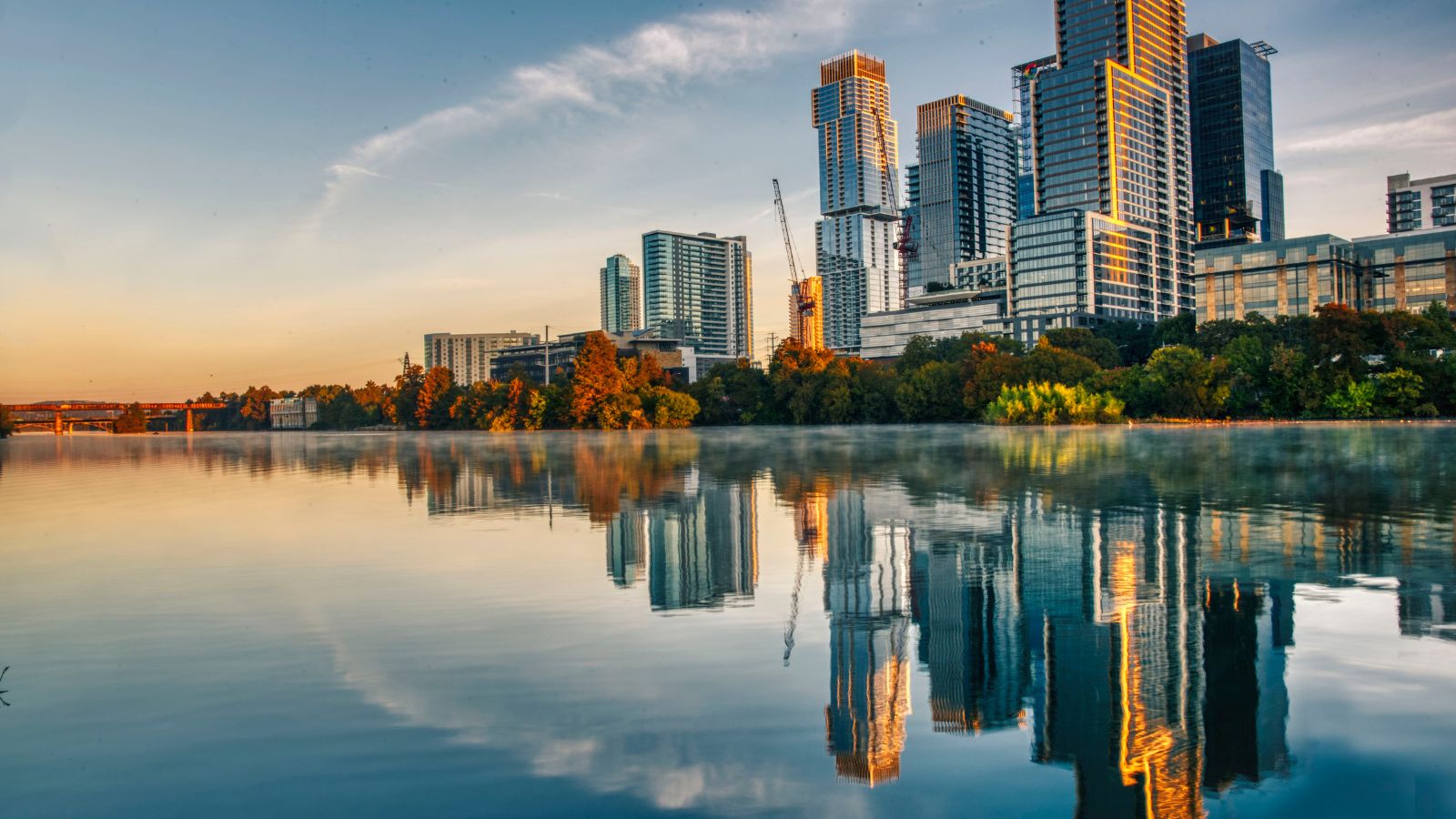 Austin buildings reflected in Lady Bird Lake in early morning light. Photograph by Luiz Simoes / Getty Images, sourced through Canva.