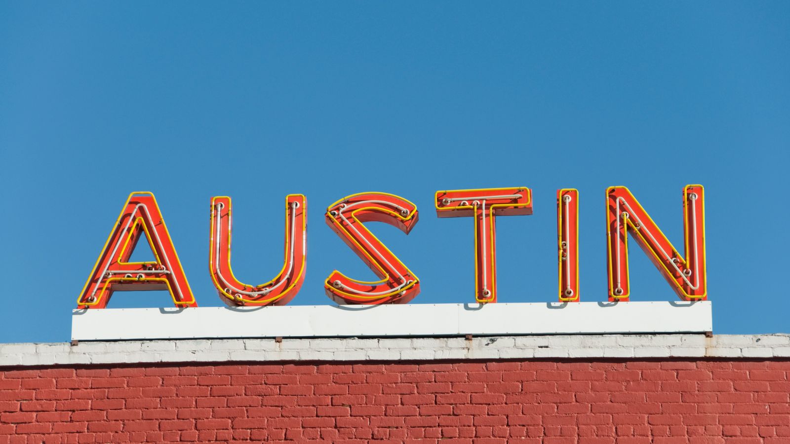Orange AUSTIN neon lettering above a red brick building against a blue sky. Photo by AustinArtist / Getty Images Signature, licensed through Canva.