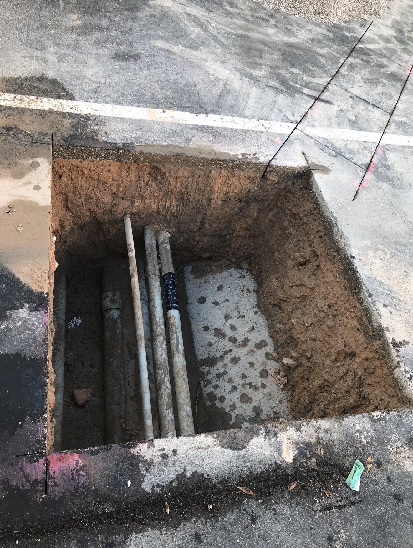 Clean square pothole excavation through asphalt exposing underground conduit