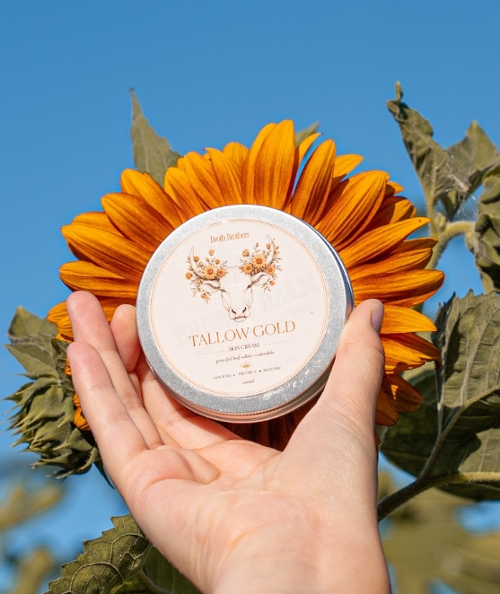 Tallow Gold Skin Cream - 100ml tin of grass-fed beef tallow and calendula held before a sunflower