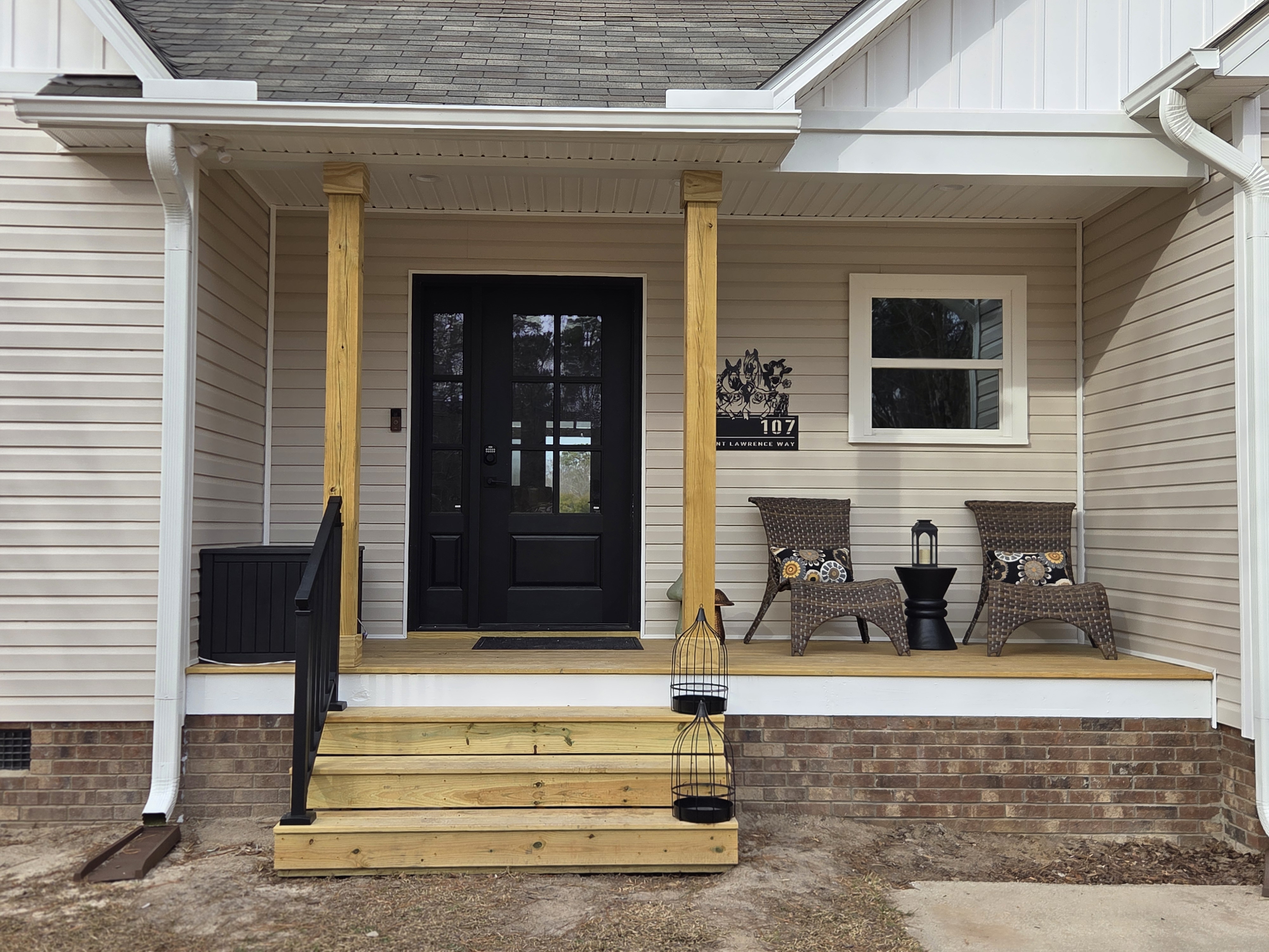 Finished covered front porch with black glass entry door, wood posts, and brick skirt on the Clayton addition