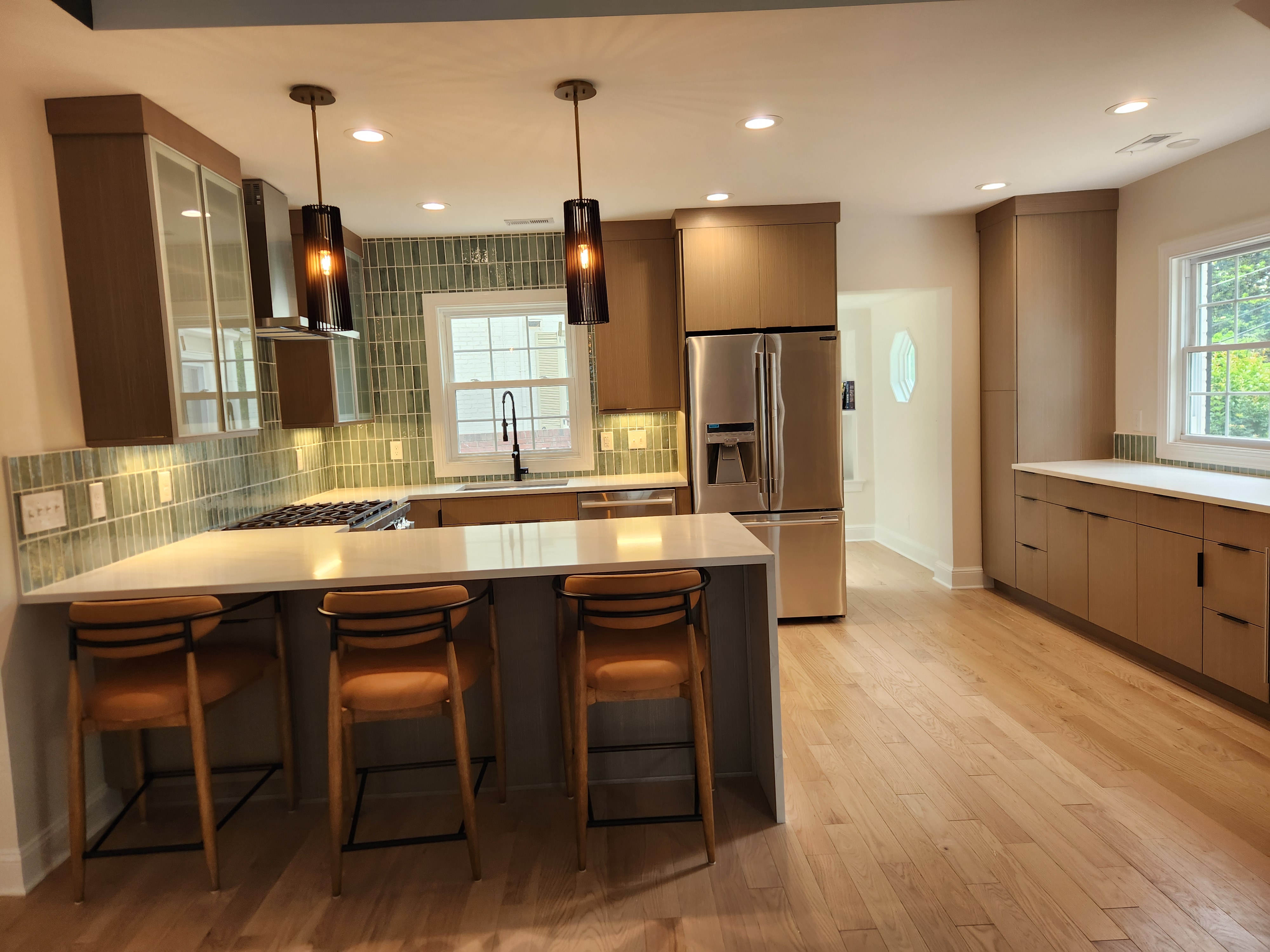 Finished Raleigh kitchen with quartz island, bar stools, green stacked tile backsplash, and stainless appliances