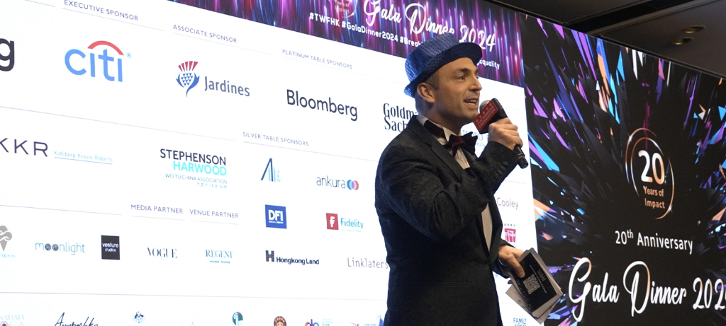 Event host on stage in front of sponsor display screen