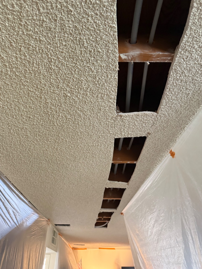 Popcorn ceiling with access holes cut for new PEX pipe installation