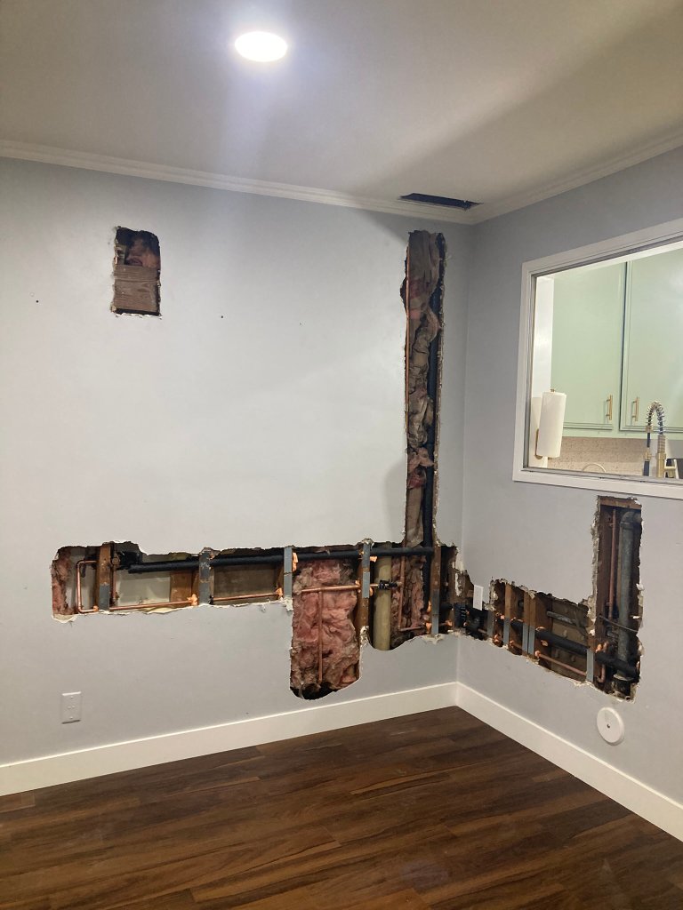 Large wall opening showing pipe replacement in dining room