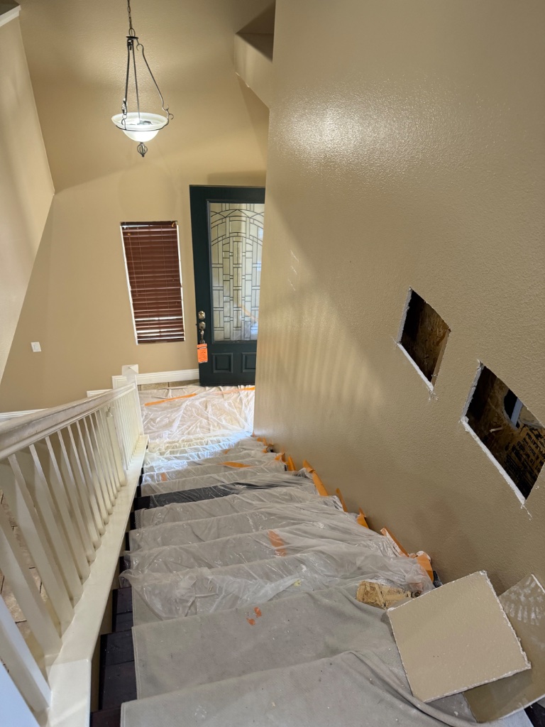 Staircase fully protected with drop cloths and wall access holes visible