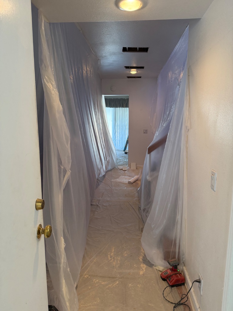 Hallway draped floor-to-ceiling in plastic — ceiling access holes for overhead pipe runs