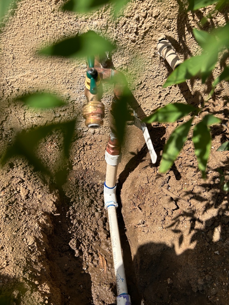 Full-length mainline trench with blue PEX replacement line and caution barrier stakes