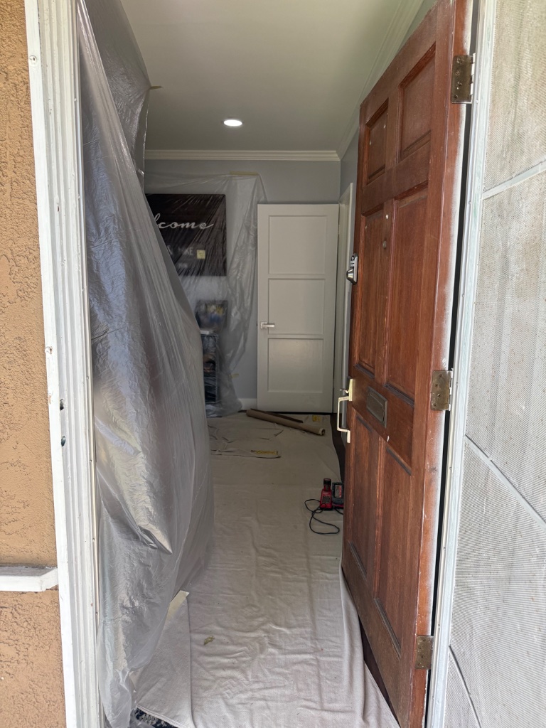 Refrigerator and white kitchen cabinets wrapped in plastic during repipe