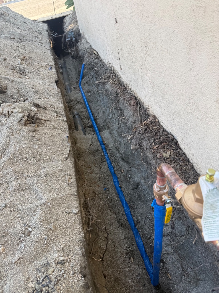 Mainline trench along foundation showing new blue PEX line with ball valve