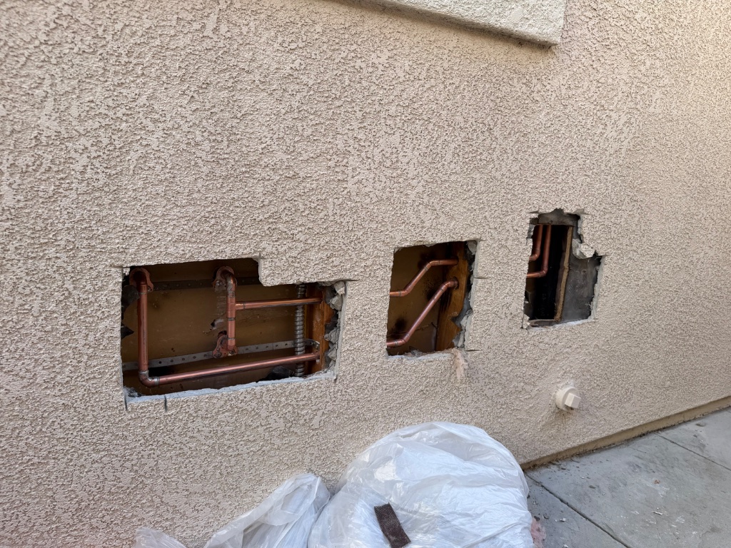 Exterior stucco wall opened in three sections to expose and replace copper piping