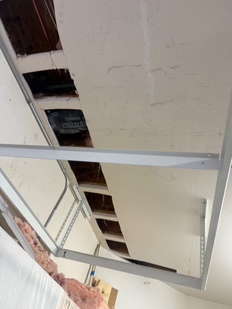 Ceiling cutout with new copper pipes, metal support bracket, and insulation visible