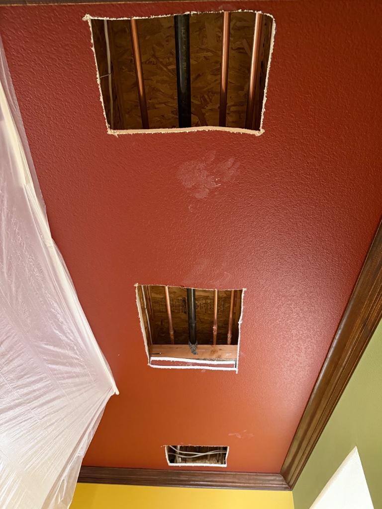 Terracotta ceiling with access holes revealing copper pipes and black drain line