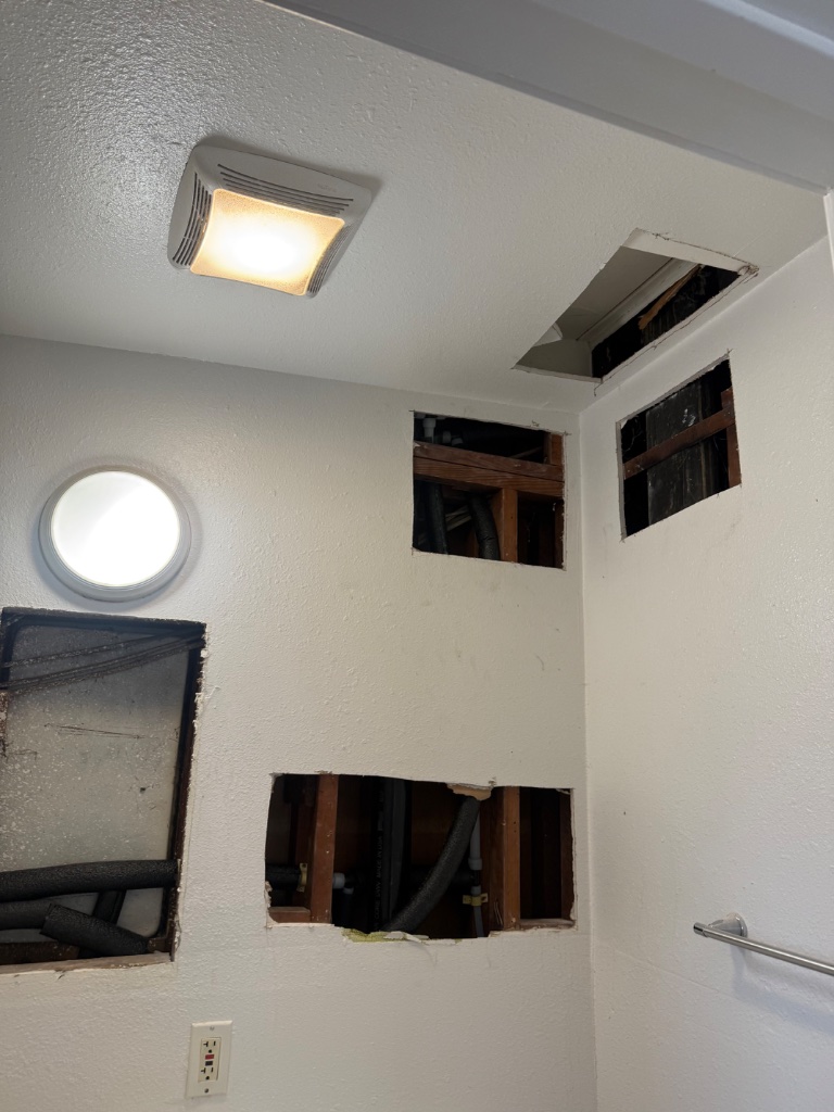 Hallway with ceiling access hole and drop cloths on floor during repipe