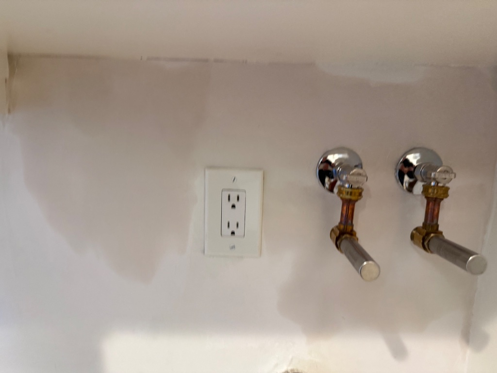 Wall patching complete — new chrome fixture stub-outs and electrical receptacle installed