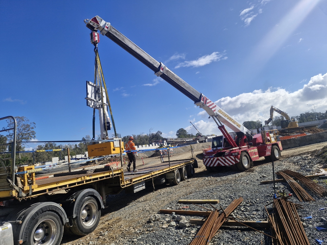 Borgers crane lifting a yellow industrial component onto a flatbed trailer on a gravel site