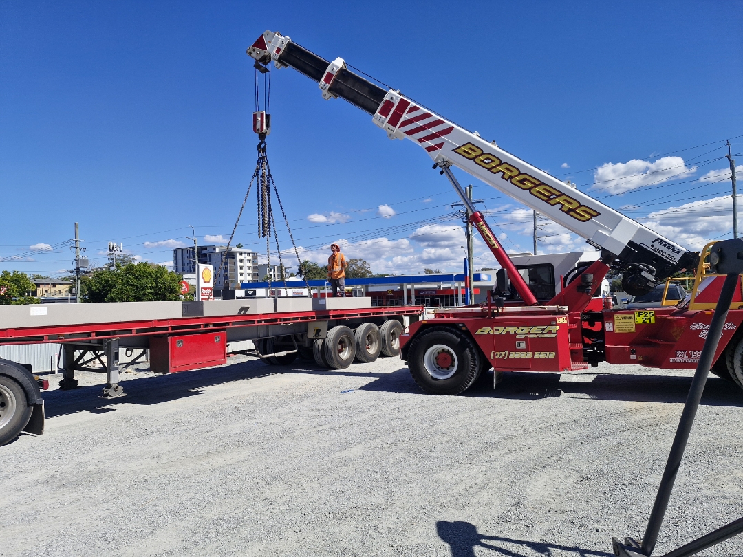 Borgers Franna crane loading a flatbed trailer on a dirt construction site