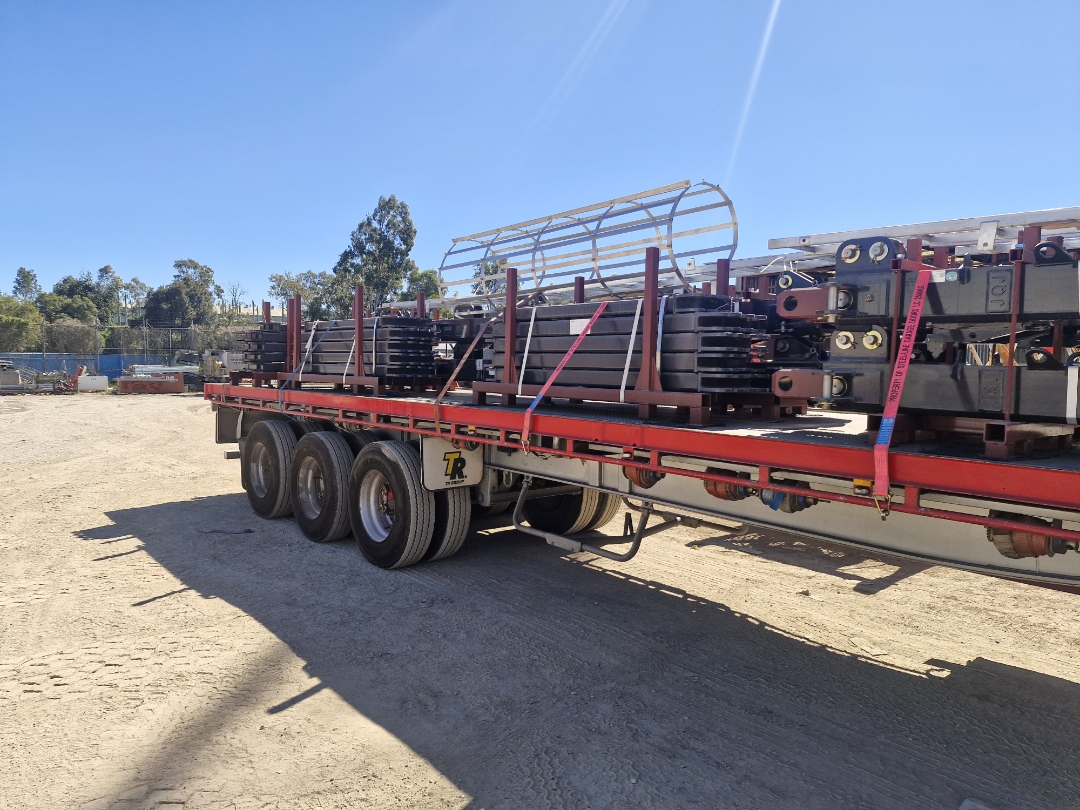 Flatbed semi-trailer loaded with heavy crane and scaffolding components at a construction yard