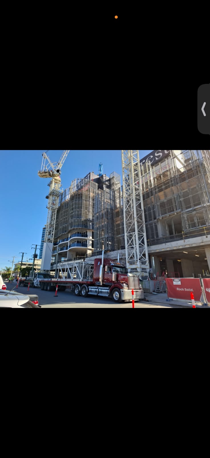 Maroon AFM semi-truck carrying a white lattice frame at a Brisbane construction site