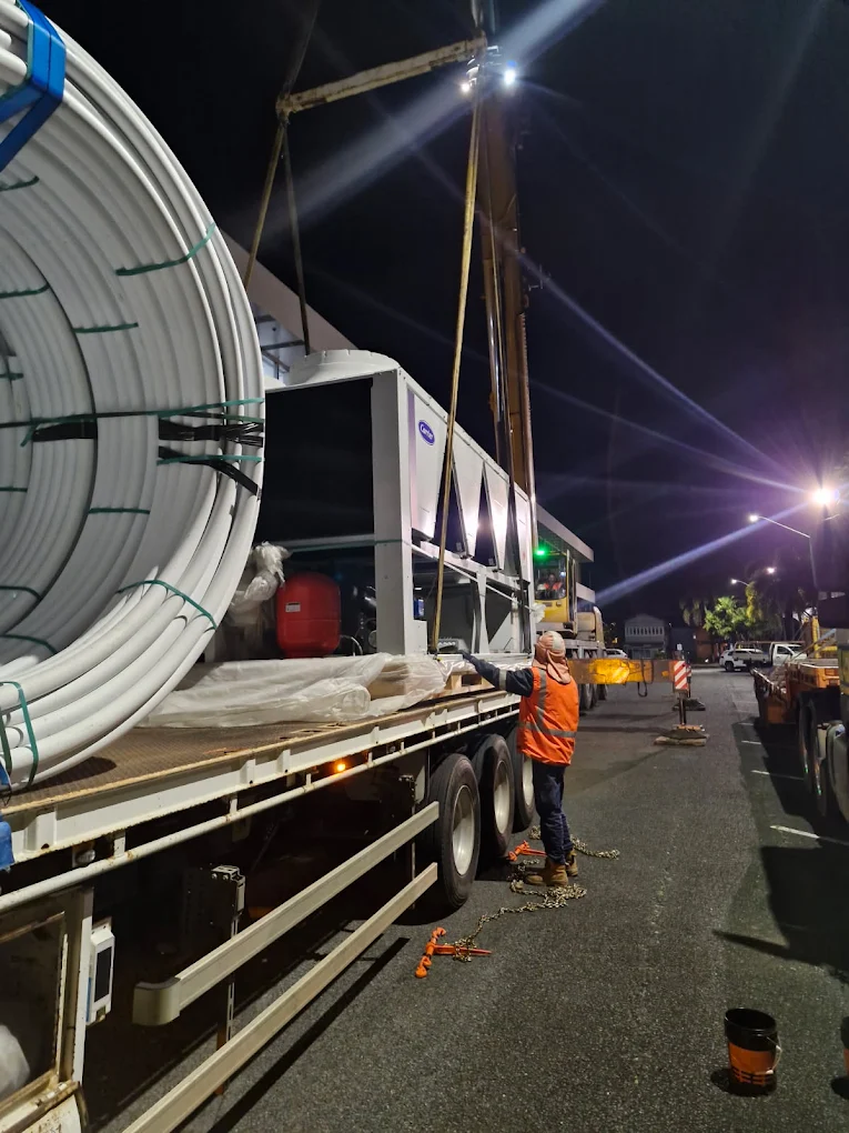 AFM driver in high-vis securing a Carrier industrial chiller unit on a flatbed at night
