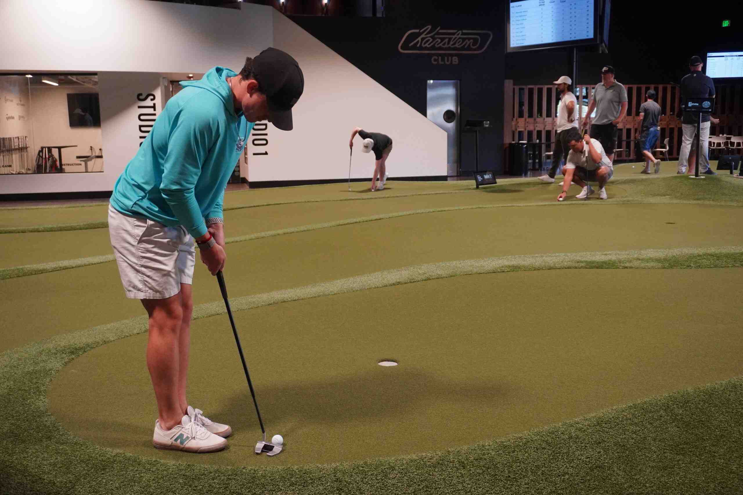 A golfer crouching low to read the line of a putt on an indoor putting green.