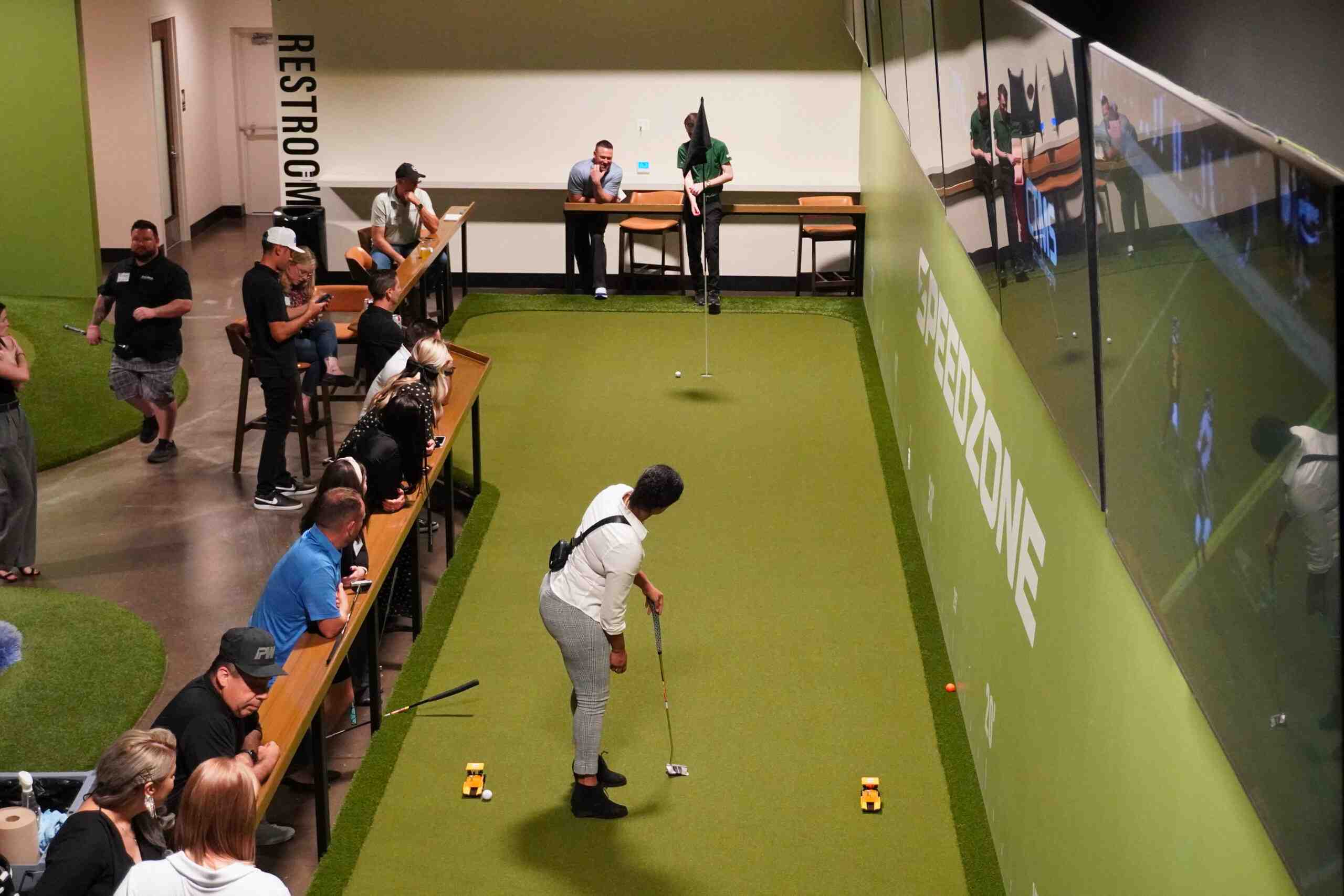 A wide view of the indoor putting course at Putting World showing real green contours and multiple holes.