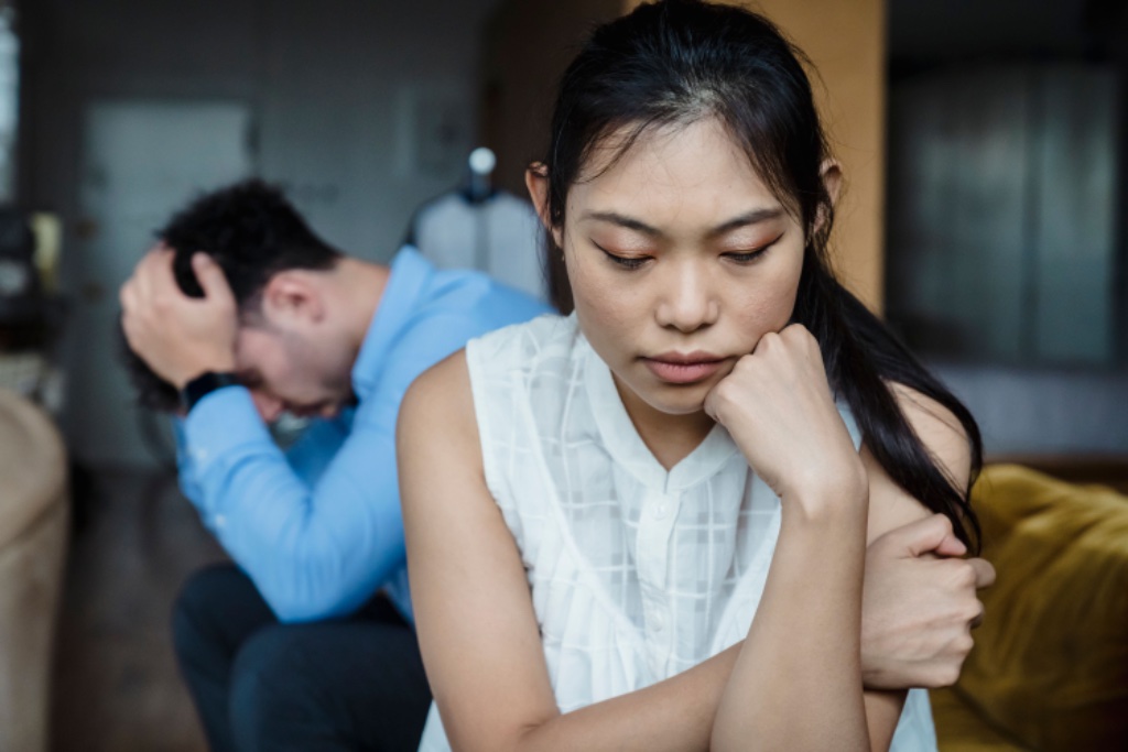 Woman looking downward, man in background — emotional distance and conflict