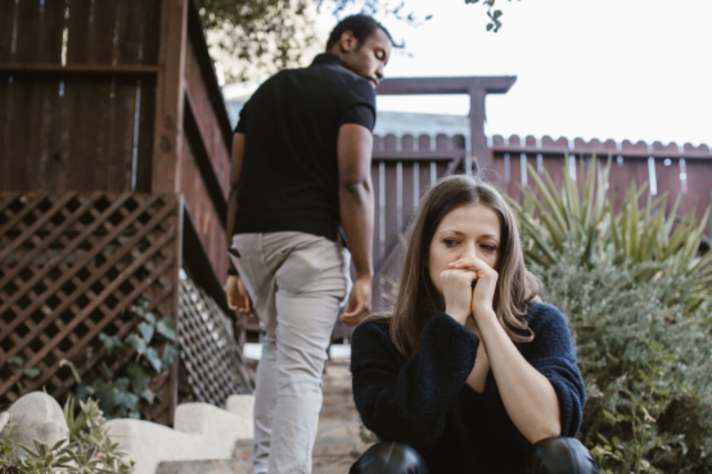 Man leaving, woman sitting alone outside — pursuit and withdrawal