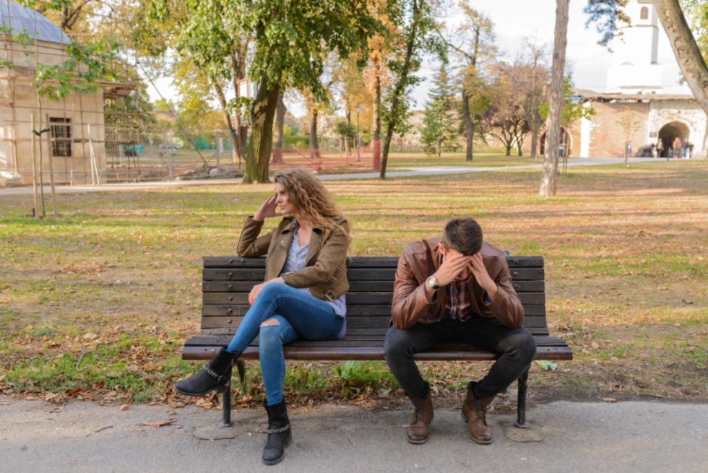 Couple sitting apart on a park bench in autumn — distance and disconnection