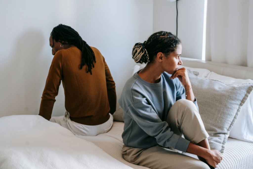 Couple sitting apart on bed, turned away from each other — emotional distance after betrayal