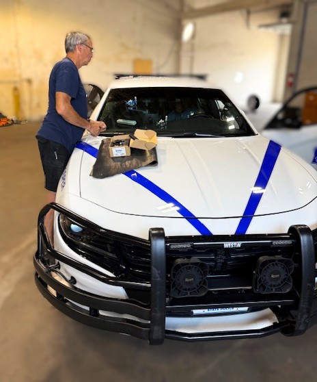 Technician replacing windshield on a white police interceptor Dodge Charger