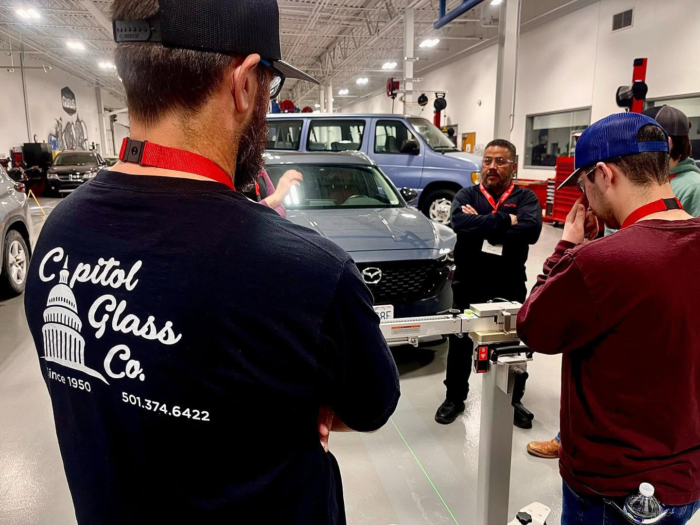 Capitol Glass technicians in the shop with a Mazda SUV during ADAS calibration, with a technician wearing a Capitol Glass Co. shirt