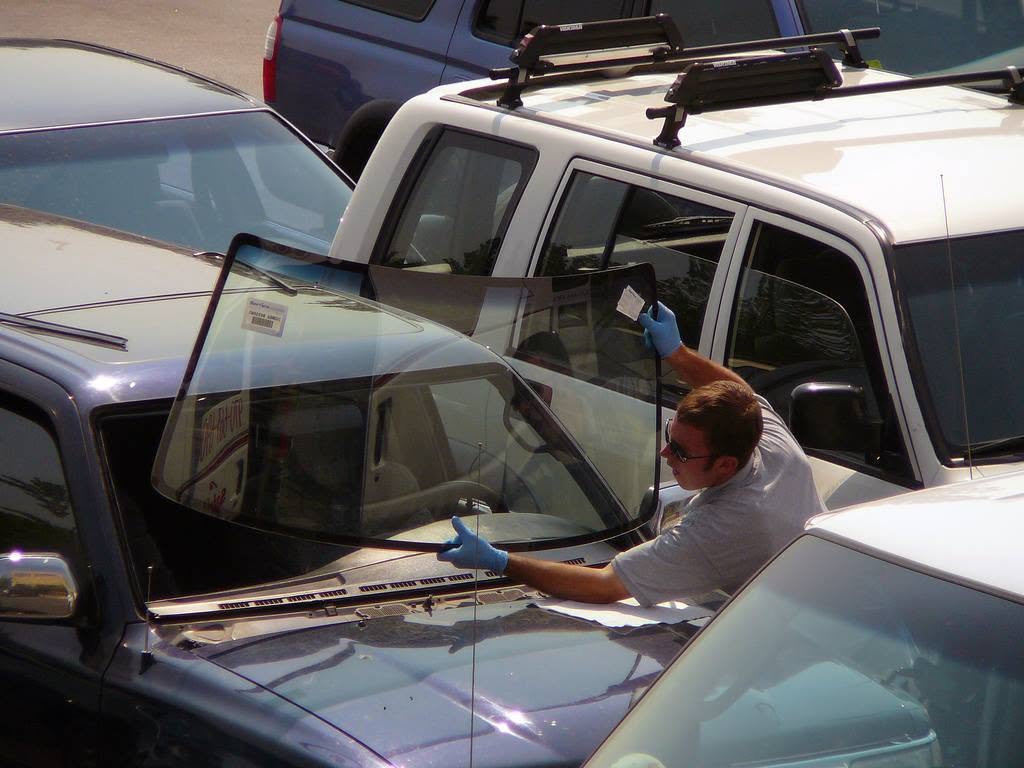 Capitol Glass technician installing a replacement windshield on a blue car in a parking lot during a mobile auto glass repair service call