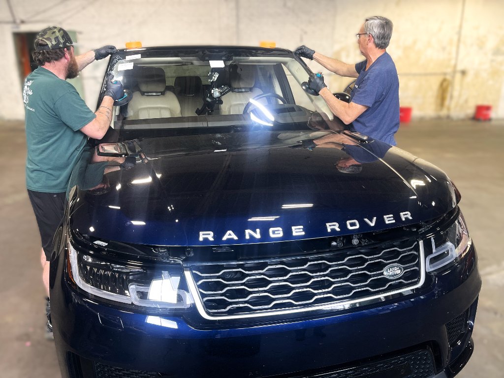 Technicians installing windshield on dark blue Range Rover Sport